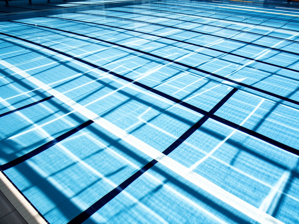 Abstract overhead view of a calm swimming pool with refracted light patterns and geometric lane lines creating a grid of blue and white, evoking structured physical space and measured effort